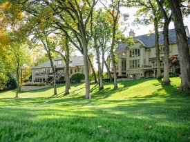 Two upscale homes on the edge of a green lawn with sun and shade from thin trees