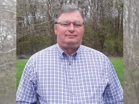 Headshot of a man in a checkered shirt with trees and grass in background