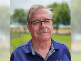 Corporate headshot of a man in a blue polo with a green grass background