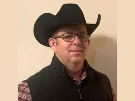Headshot of a man in a black cowboy hat and a black vest with red and white shirt. 