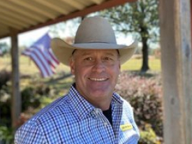Man in a cowboy hat and checkered shirt smiling at camera 
