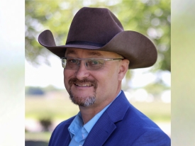 Corporate headshot of a man in a brown cowboy hat with blue blazer and shirt 