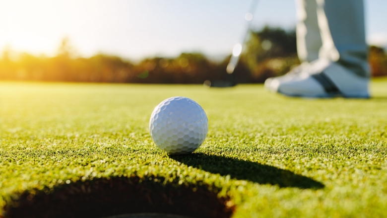 Golfer putting golfball into cup on putting green.