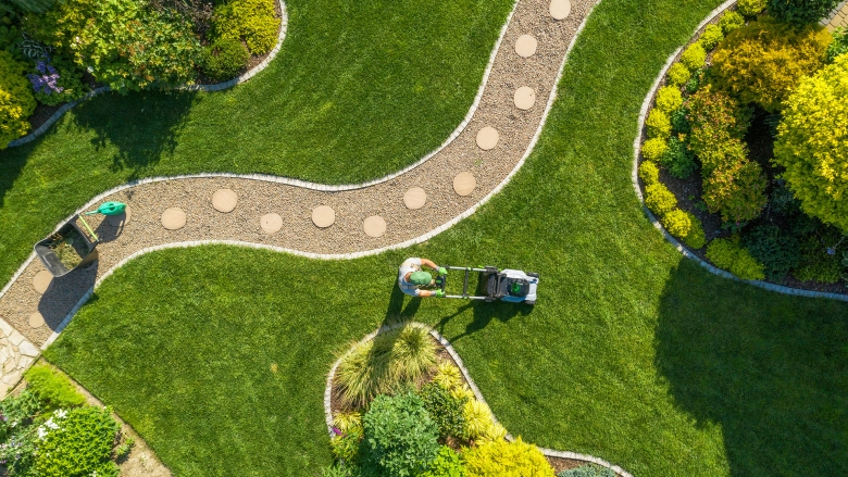 Overhead view of landscaper mowing a yard with grass, bushes, and path