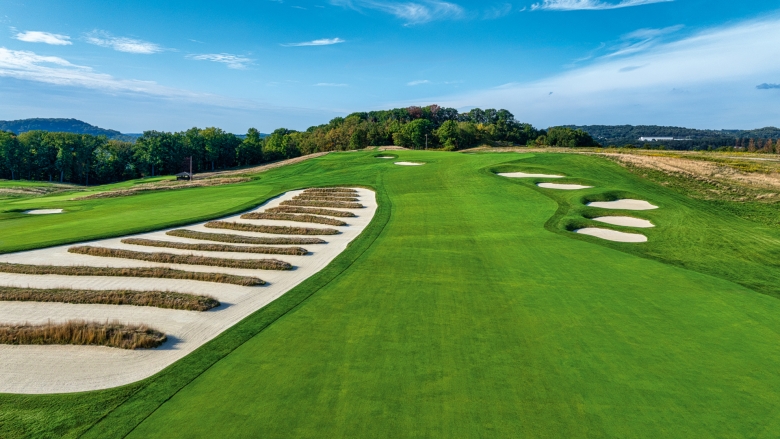 Green golf course with "church pew" style bunkers and blue sky. 
