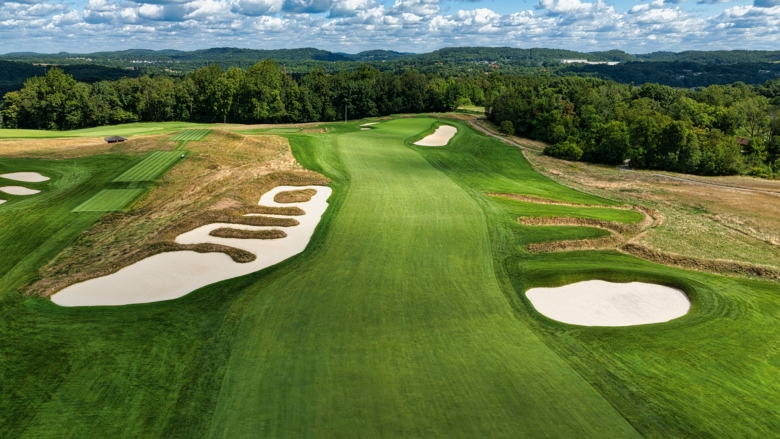 Green golf course with rugged terrain and trees in the background. 