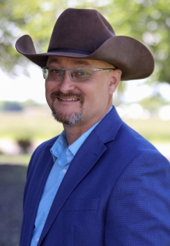 Corporate headshot of a man in a brown cowboy hat with blue blazer and shirt 