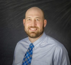 Headshot of a man in a grey shirt on a black background