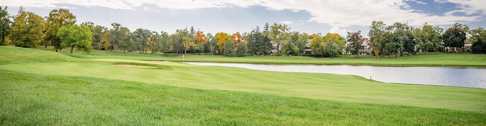 Golf course with a lake and trees in the distance. 