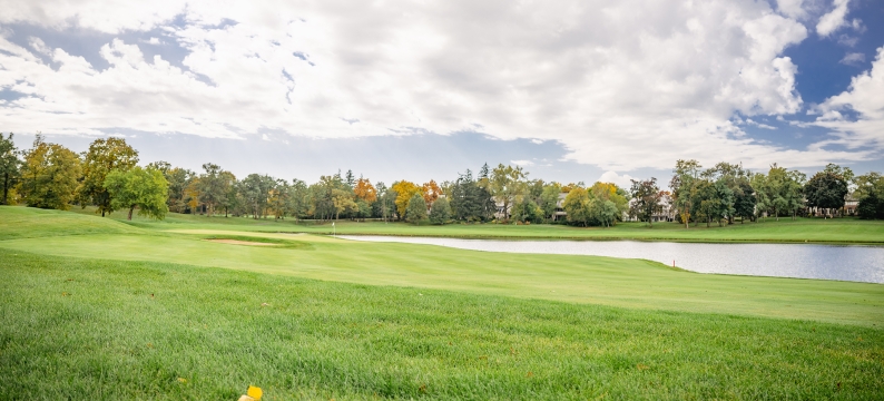 Golf course with a lake and trees in the distance. 