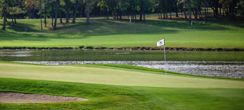 Golf hole with flag, green grass and water 