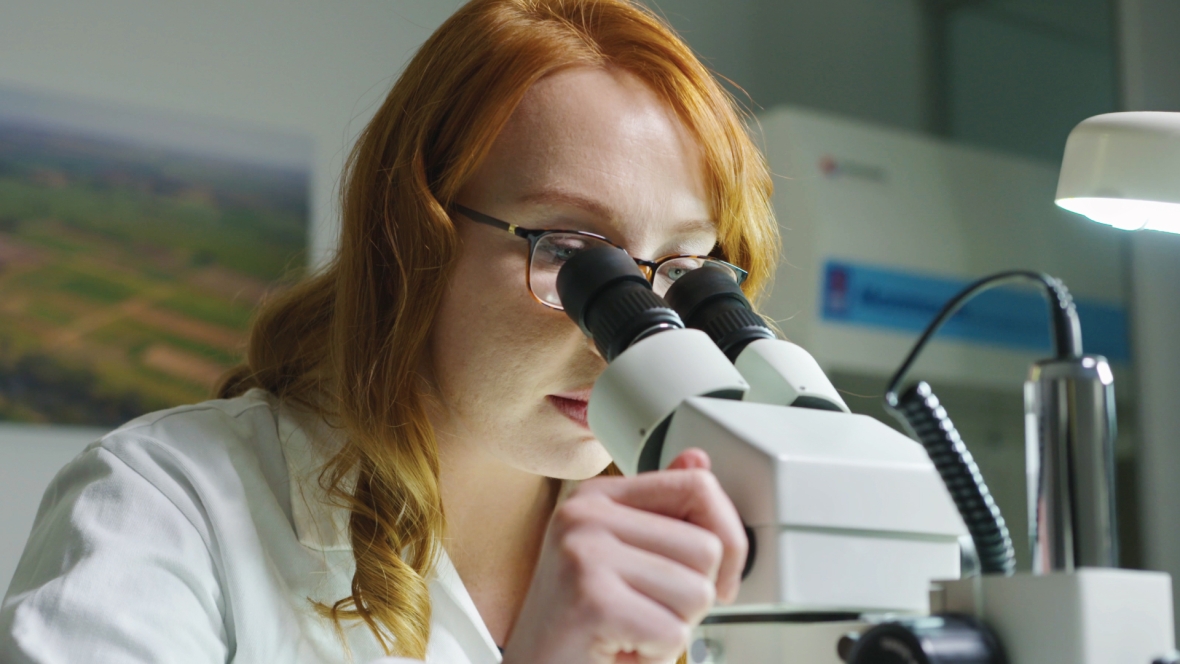 Women in lab coat looking through a microscope.