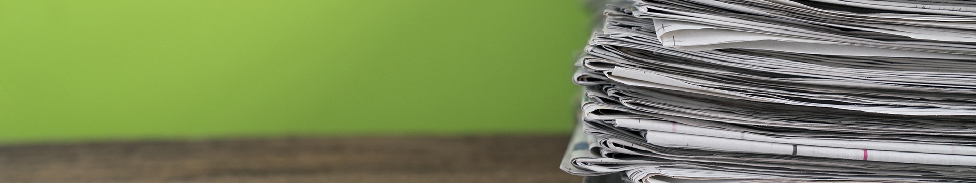Stack of newspapers against a lime green wall 
