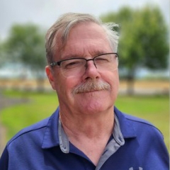 Corporate headshot of a man in a blue polo with a green grass background