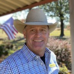 Man in a cowboy hat and checkered shirt smiling at camera 