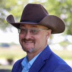 Corporate headshot of a man in a brown cowboy hat with blue blazer and shirt 